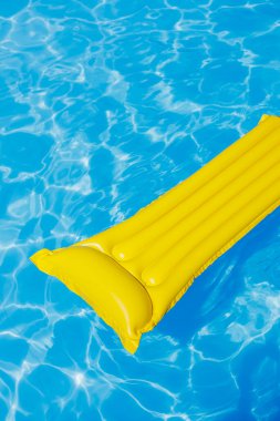 Sarı bir şişme yatak boş bir mavi su havuzunda yüzer. Yaz tatili kavramı