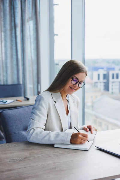 Pretty business woman looking through notebook, focused on work, freelancer, remote work, studying study, modern office, indoor social distancing. Woman in office with glasses and laptop