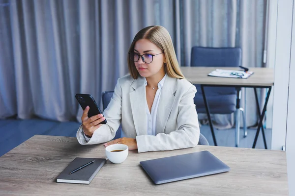 Blogger woman with digital mobile phone smiling during coffee break in cafe interior, happy european woman with smartphone and caffeine drink posing