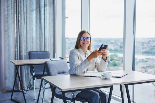 Blogger woman with digital mobile phone smiling during coffee break in cafe interior, happy european woman with smartphone and caffeine drink posing