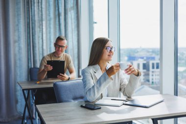 Manager woman in glasses doing office work and smiling, successful female boss in optical glasses for vision correction, posing at the table. In the background a man
