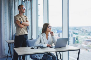 Gözlüklü kadın ofis işi yapıyor ve gülümsüyor, görüş düzeltmesi için optik gözlüklü başarılı bayan patron masada poz veriyor. Arka planda bir adam