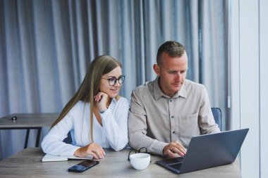 Businessmen are discussing while working with laptop in the office. Focused business people cooperating in a modern workspace. Two young businessmen are sitting together at a table.