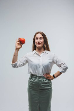 Elinde kırmızı bir elma tutan gülümseyen kadın. Beyaz gömlekli güzel bir esmer. Sağlıklı bitkiler ve vitaminler. Beyaz arkaplan.