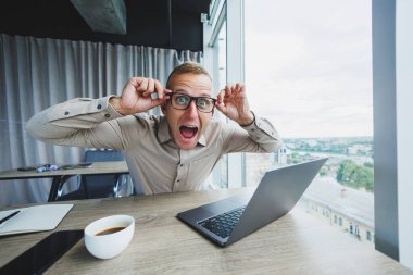 İş yerinde kameraya bakan duygusal bir adam, gözlüklü bir adam, bilgisayarlı bir masada oturuyor, bir öğrenci bir ofis kafesinde yeni fikirler için ilham arıyor.