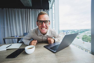 İş yerinde kameraya bakan duygusal bir adam, gözlüklü bir adam, bilgisayarlı bir masada oturuyor, bir öğrenci bir ofis kafesinde yeni fikirler için ilham arıyor.