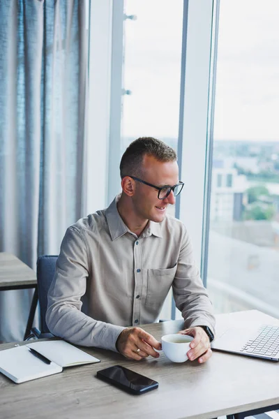 A businessman works on a laptop, a manager sits at a table in the office, works on a laptop. Freelancer workplace, employee at remote work. Remote workplace in coworking, cafe