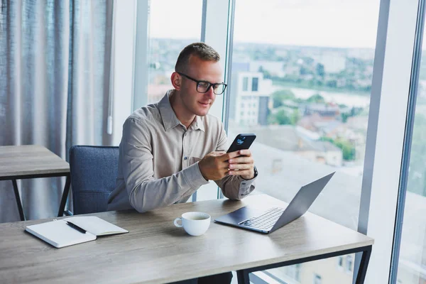 Successful man talking on smartphone and browsing netbook while surfing internet in office at table