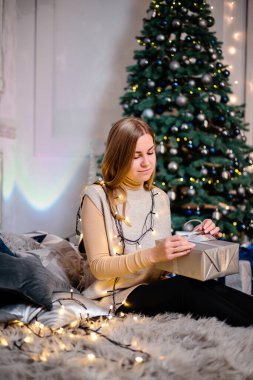 Uzun, güzel saçlı genç bir kadın Noel hediyelerinin önünde oturur ve güler. Mutlu yıllar.