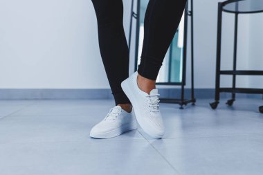 Women's legs close-up in white leather sneakers made from natural leather.Collection of women's summer shoes