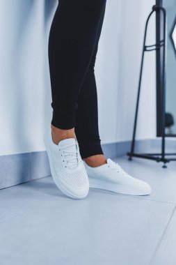 Women's legs close-up in white leather sneakers made from natural leather.Collection of women's summer shoes