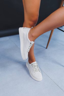 Women's legs close-up in white leather sneakers made from natural leather.Collection of women's summer shoes