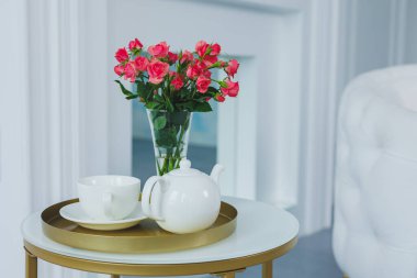 A table with a white teapot and a white cup. on the table a vase with fresh flowers