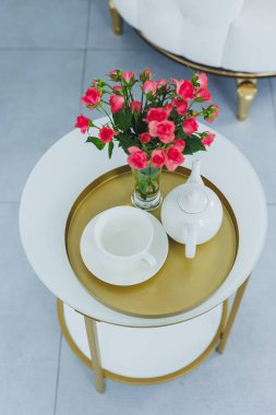 A table with a white teapot and a white cup. on the table a vase with fresh flowers