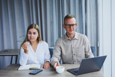 Young business team, male and female colleagues talking at work, discussing a new project with a laptop, young executives having a friendly conversation, collaborating in teamwork in the office