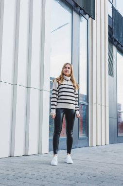 A woman in a warm sweater and black leather leggings in white autumn sneakers. Women's shoes made of genuine leather