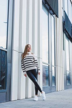 A woman in a warm sweater and black leather leggings in white autumn sneakers. Women's shoes made of genuine leather