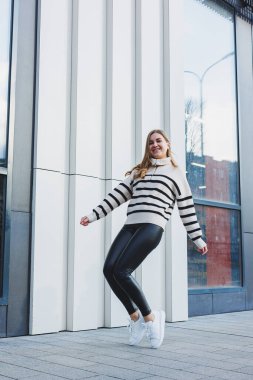 A woman in a warm sweater and black leather leggings in white autumn sneakers. Women's shoes made of genuine leather