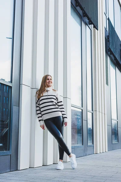 A woman in a warm sweater and black leather leggings in white autumn sneakers. Women's shoes made of genuine leather