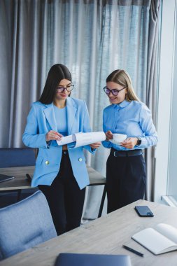 Two young women managers work in a modern office. Women colleagues are talking while working. Friendly staff