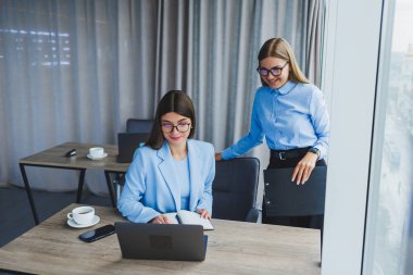 Busy business women with a laptop in the office, watching content on the laptop and discussing the project together, sitting in the office during a working break. Teamwork, corporate discussion
