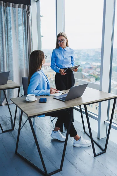 Busy business women with a laptop in the office, watching content on the laptop and discussing the project together, sitting in the office during a working break. Teamwork, corporate discussion