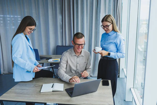 Successful young business people laughing while collaborating on a new project in the office. Group of diverse business people using laptop while working together in modern workspace.