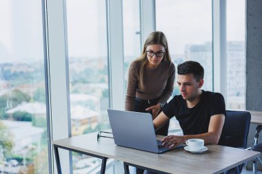 İş kadını ve iş adamı laptopta bir şey arıyorlar. İş birliği ve takım çalışması kavramı. Ofisteki masada gülümseyen genç milenyumlar. Modern başarılı insanlar