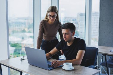 İş kadını ve iş adamı laptopta bir şey arıyorlar. İş birliği ve takım çalışması kavramı. Ofisteki masada gülümseyen genç milenyumlar. Modern başarılı insanlar