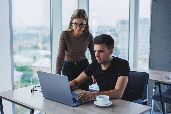 Business woman and businessman are looking for something in the laptop. The concept of business cooperation and teamwork. Young smiling millennials at the table in the office. Modern successful people