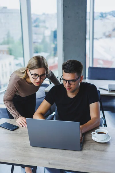 Business woman and businessman are looking for something in the laptop. The concept of business cooperation and teamwork. Young smiling millennials at the table in the office. Modern successful people