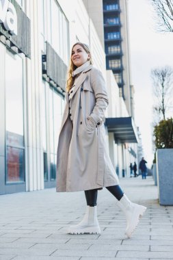 Bej renkli yağmurluk ve sonbahar deri çizmeleri içinde caddede yürüyen tatlı genç bir kadın. Sonbahar ılık görüntüsü. Kadın modası