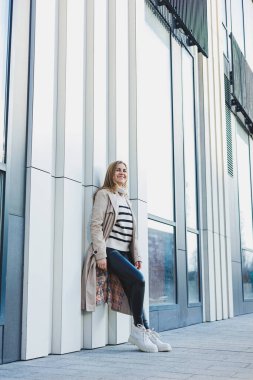 Bej renkli yağmurluk ve sonbahar deri çizmeleri içinde caddede yürüyen tatlı genç bir kadın. Sonbahar ılık görüntüsü. Kadın modası