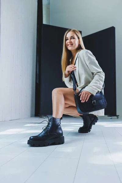 Stylish woman in classic beige clothes with trendy black leather bag in stylish shoes. Beautiful female legs with black shoes in the studio