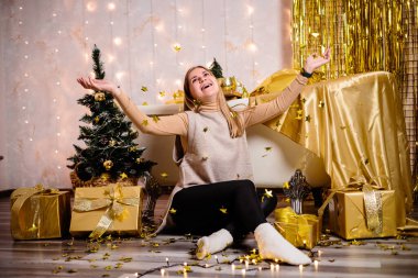 Yeni yıl odasında mutlu bir kadın. Odanın altın renginde yeni yıl süslemesi. Bayram ve festival tasarımı konsepti. Yeni yıl için ev dekorasyonu.