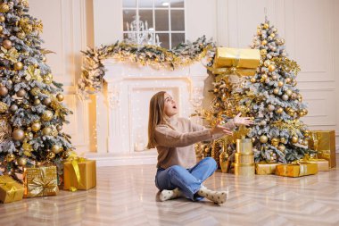 Genç ve mutlu bir kadın yeni yıl hediyesiyle oturuyor. Noel ağacı ve süslü çelenkleri olan bir şömine. Yeni yıl havası.
