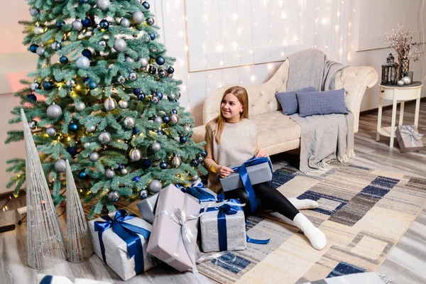 Boldog Fiatal Egy Ajándékkal Karácsonyfa Mellett Fehér Ezüst Színű Kanapé — Stock Fotó