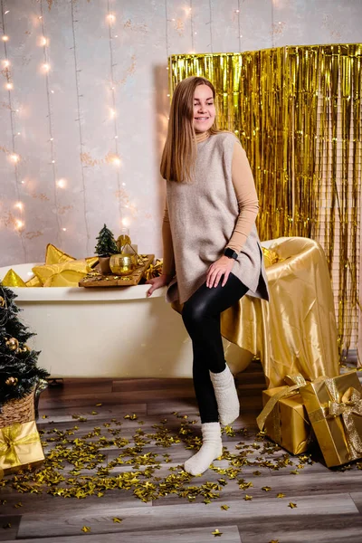 Happy woman in New Year's room. New Year's decoration of the room in golden color. The concept of the holiday and festive design. Home decor for the New Year.
