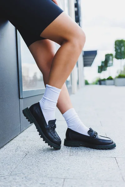 Female legs in leather shoes, white socks with and black moccasins, black shorts, fashion details