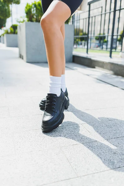 Female legs in leather shoes, white socks with and black moccasins, black shorts, fashion details