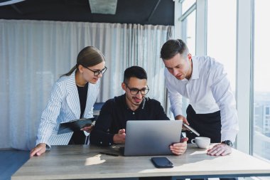 Resmi olarak bir grup iş adamı proje detaylarını tartışıyor ve modern bir toplantı odasında iş birliği yaparken dizüstü bilgisayar ekranına bakıyor. Modern ofis