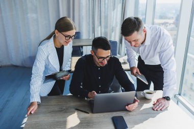 Resmi olarak bir grup iş adamı proje detaylarını tartışıyor ve modern bir toplantı odasında iş birliği yaparken dizüstü bilgisayar ekranına bakıyor. Modern ofis