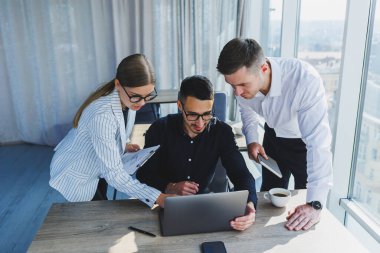 Resmi olarak bir grup iş adamı proje detaylarını tartışıyor ve modern bir toplantı odasında iş birliği yaparken dizüstü bilgisayar ekranına bakıyor. Modern ofis