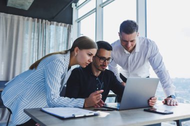 Resmi olarak bir grup iş adamı proje detaylarını tartışıyor ve modern bir toplantı odasında iş birliği yaparken dizüstü bilgisayar ekranına bakıyor. Modern ofis