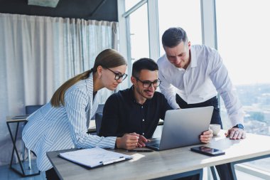 Resmi olarak bir grup iş adamı proje detaylarını tartışıyor ve modern bir toplantı odasında iş birliği yaparken dizüstü bilgisayar ekranına bakıyor. Modern ofis