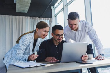 Resmi olarak bir grup iş adamı proje detaylarını tartışıyor ve modern bir toplantı odasında iş birliği yaparken dizüstü bilgisayar ekranına bakıyor. Modern ofis
