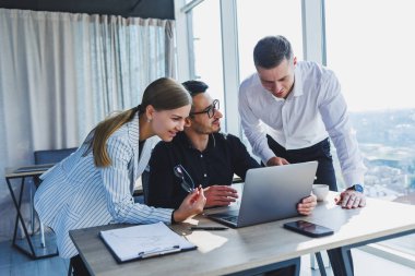 Resmi olarak bir grup iş adamı proje detaylarını tartışıyor ve modern bir toplantı odasında iş birliği yaparken dizüstü bilgisayar ekranına bakıyor. Modern ofis