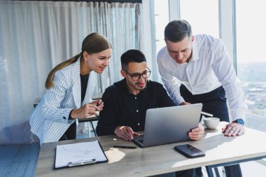 Resmi olarak bir grup iş adamı proje detaylarını tartışıyor ve modern bir toplantı odasında iş birliği yaparken dizüstü bilgisayar ekranına bakıyor. Modern ofis