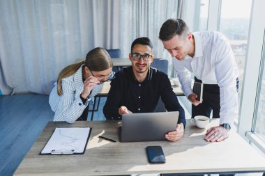 Resmi olarak bir grup iş adamı proje detaylarını tartışıyor ve modern bir toplantı odasında iş birliği yaparken dizüstü bilgisayar ekranına bakıyor. Modern ofis