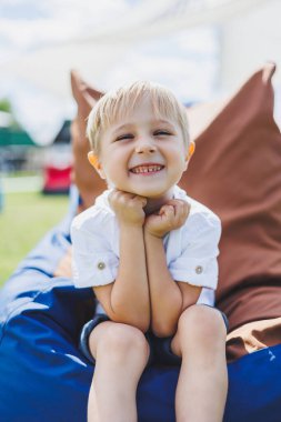 Mutlu çocuk yaz parkında koltukta oturuyor. Beyaz tişörtlü küçük bir çocuk dışarıda eğleniyor. Çocukluk ve mutluluk.